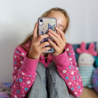 Symbolfoto zum Thema Handynutzung bei Kindern: Ein Mädchen sitzt in ihrem Bett und ist am Handy.