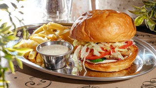 Burger mit Pommes auf einem silbernen Tablett: Eine Studie führt ein gesteigertes Risiko für 32 Erkrankungen auf den Verzehr von hochverarbeiteten Lebensmitteln zurück, darunter Diabetes Typ 2, Adipositas, Herzinfarkt oder Krebs. 