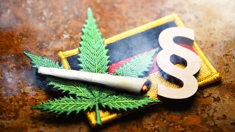 Cannabisblatt-Symbol, Joint, Paragrafenzeichen auf Deutschlandfahne: Das Cannabisgesetz wird evaluiert. Erste Ergebnisse zeigen: Mehr konsumiert wird nicht. Probleme bereiten die vielen Telemedizin-Plattformen, die die Verschreibungen sehr leicht machen.