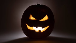 Dunkler Halloween-Kürbis mit gruseligem Gesicht: Ob The Shining, True Crime oder das Horror-Maislabyrinth an Halloween: Viele gruseln sich gern und lieben den Nervenkitzel. Gruseln kann uns sogar gut tun.