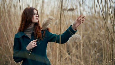 Junge Frau steht in einem Feld und berüht mit der Hand einen Halm: Sind hochsensible Menschen empfindsam oder einfach nur empfindlich?
