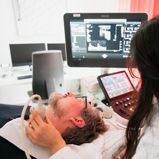 Dr. Eckart von Hirschhausen wird von Neurologin Dr. Taraneh Ebrahimi mit Ultraschall auf Plaque untersucht – eine mögliche Ursache für vaskuläre Demenz, die zweithäufigste Erscheinungsform der Demenz. – ARDWDR HIRSCHHAUSEN UND DAS GROßE VERGESSEN