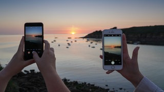 Sonnenuntergang am Strand in der Bretagne, fotografiert von zwei Smartphones: Kann man auf Fotos eigentlich erkennen, ob die Sonne gerade aufgeht oder ob sie untergeht?