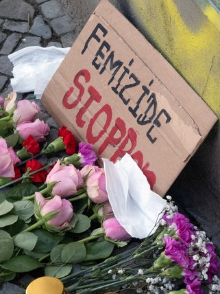 Blumen, niedergelegt für das Opfer eines Femizids. Auf einem Schild steht: "Femizide stoppen". Jedes Jahr versuchen in Deutschland geschätzt hunderte Männer ihre Partnerinnen und Ex-Partnerinnen zu ermorden, fast jeden zweiten Tag stirbt eine Frau.