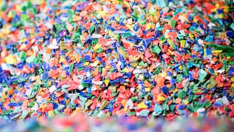 Symbolfoto: Buntes Plastikgranulat liegt in einer Halle in einem Behälter