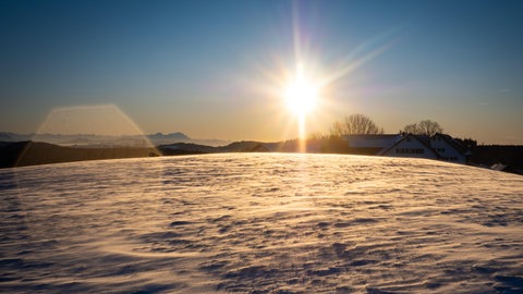 Sonnenuntergang an einem eisigen Winterabend, es liegt viel Schnee auf den Feldern.
