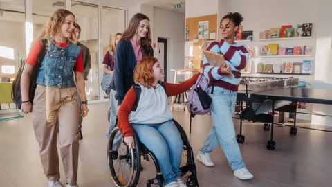 Schülerinnen, eine davon im Rollstuhl, auf dem Flur einer Schule: Eltern haben die Wahl, wo ihr Kind mit Förderbedarf zur Schule gehen soll. Doch Inklusion an Schulen hapert immer noch an baulichen Einschränkungen, fehlendem Personal, am Geld.