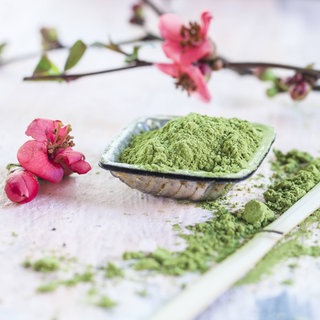 Matcha-Pulver, rosa Blüten und ein Matcha-Löffel aus Bambus: Kurzfristig steigert grüner Tee die Konzentrationsfähigkeit, oft auch die Stimmung, das Koffein kann leicht euphorisierend wirken. Krankheiten beugt er allein nicht vor. 