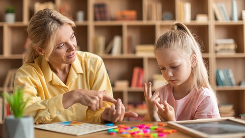 Kleines Mädchen rechnet mühsam mit den Fingern, eine Lehrerin hilft: Die Rechenstörung Dyskalkulie betrifft viele Kinder. Eigentlich gibt es gute Therapien und Hilfen, nur werden die oft nicht angewandt.