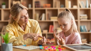 Kleines Mädchen rechnet mühsam mit den Fingern, eine Lehrerin hilft: Die Rechenstörung Dyskalkulie betrifft viele Kinder. Eigentlich gibt es gute Therapien und Hilfen, nur werden die oft nicht angewandt.