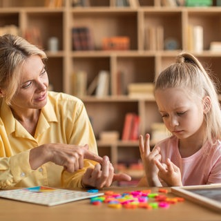 Kleines Mädchen rechnet mühsam mit den Fingern, eine Lehrerin hilft: Die Rechenstörung Dyskalkulie betrifft viele Kinder. Eigentlich gibt es gute Therapien und Hilfen, nur werden die oft nicht angewandt.