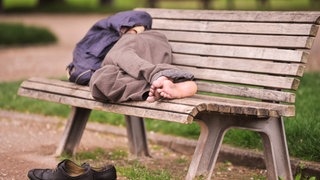 Obdachloser schläft auf einer Parkbank: Die beste Strategie gegen Obdachlosigkeit ist, sie zu verhindern. Kommunen können Menschen helfen, wenn der Verlust der Wohnung droht. Neben Wohnraum brauchen Obdachlose Sinn im Leben.