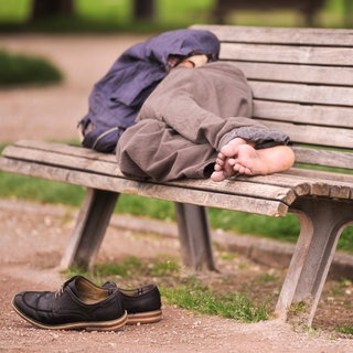 Obdachloser schläft auf einer Parkbank: Die beste Strategie gegen Obdachlosigkeit ist, sie zu verhindern. Kommunen können Menschen helfen, wenn der Verlust der Wohnung droht. Neben Wohnraum brauchen Obdachlose Sinn im Leben.