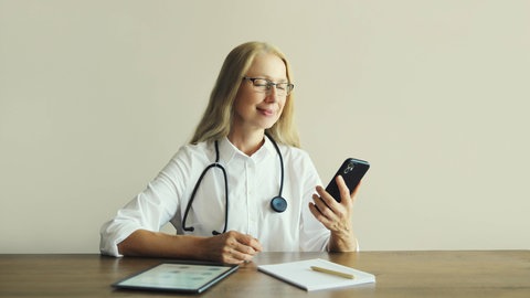 Eine Ärztin sitzt mit Tablet und Handy am Tisch