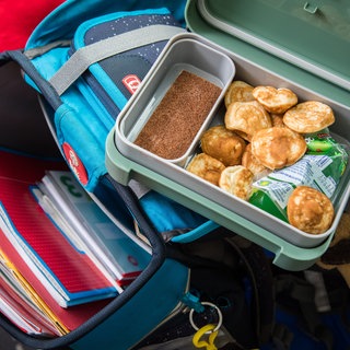 Eine geöffnete Brotdose ist auf einem Schulranzen zu sehen (gestellte Szene).