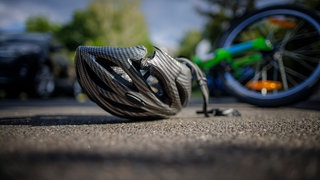 Symbolfoto zum Thema Fahrradunfall (gestellte Szene). Ein zerbrochener Fahrradhelm liegt neben einem Fahrrad auf einer Strasse. 