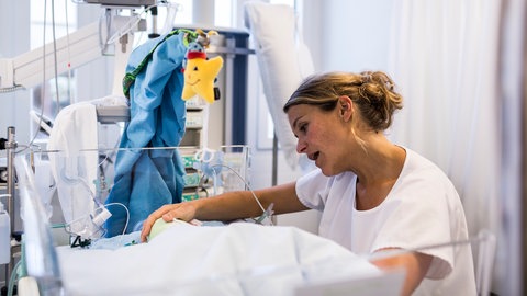 Eine Pflegefachkraft singt einem Baby etwas vor, um die Entwicklung des Frühgeborenen durch eine Musiktherapie zu unterstützen (August 2013,  Neonatologie-Intensivstation, Universitätsspital Zürich)