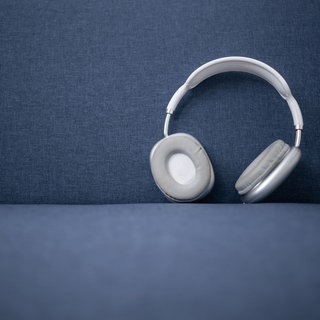 Weiße und graue kabellose Kopfhörer auf einem blauen Sofa