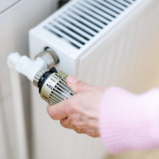 Eine Frau stellt an einem Thermostaten die Temperatur von einem Heizkörper ein.