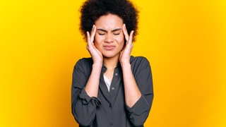 Frau fasst sich mit schmerzverzerrtem Gesicht an die Schläfen: 2025 kommen neue Medikamente auf den deutschen Markt, die spezifisch das Migräne auslösende Eiweiß blockieren, auch prophylaktisch. 