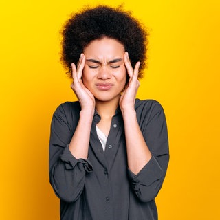 Frau fasst sich mit schmerzverzerrtem Gesicht an die Schläfen: 2025 kommen neue Medikamente auf den deutschen Markt, die spezifisch das Migräne auslösende Eiweiß blockieren, auch prophylaktisch. 