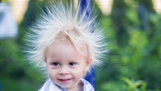 Kleiner blonder Junge. Seine Haare sind statisch geladen und stehen rund um seinen Kopf in die Höhe: Warum sind wir manchmal elektrisch aufgeladen)