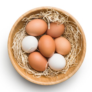 Schale mit weißen und braunen Eiern auf beigefarbenem Ostergras: Wovon hängt die Farbe der Eier ab?