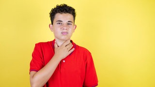 Junge hält sich den Hals: Das Wort "Stimmbruch" ist eigentlich eine Täuschung, denn anatomisch gesehen bricht gar nichts. Es geht auch nichts kaputt, es reißt nichts. Das einzige, was bricht, ist der Klang. Warum passiert das?