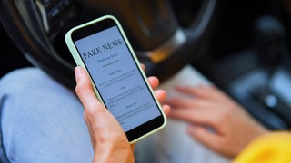 Symbolfoto: Eine Person liest "Fake News" auf dem Handy.