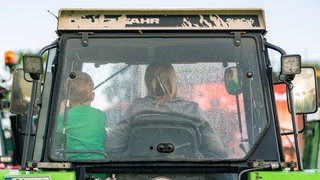 Eine Landwirtin und ihr kleiner Sohn fahren in ihrem Trecker: Die Herausforderungen für Frauen auf Höfen sind enorm: Sie müssen die harte landwirtschaftliche Arbeit erledigen, Kinder erziehen, ältere Angehörige pflegen, Generationenkonflikte bewältigen. 