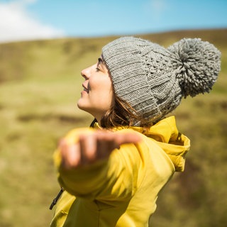 Junge Frau breitet in der Natur die Arme aus: Was ist Glück und wie können wir es finden?