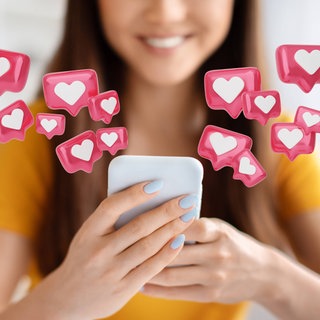 Junge Frau schaut glücklich lächelnd auf ihr Smartphone, aus dem Herzen fliegen: Bewusstes Dopamintraining mit genügend Schlaf, Pausen und echten Zielen statt Likes und Push-Nachrichten stabilisiert uns im digitalen Alltag.