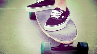 Füße in Turnschuhen auf einem alten Skateboard: Wer hat das Skateboard erfunden?