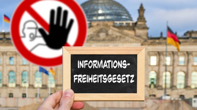 Hand mit Tafel vor dem Reichstagsgebäude, darauf der Schriftzug "Informationsfreiheitsgesetz". Im Hintergrund ein Warnschild mit erhobener Hand: Um die Informationsfreiheit steht es in Deutschland nicht besonders gut