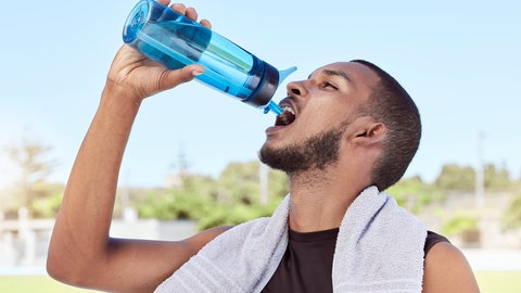 Ein Mann trinkt beim Training aus einer Wasserflasche: Ohne nachzudenken, schlucken wir etwa 2.000 Mal pro Tag: wenn wir essen und trinken oder den Speichel, der Mund und Zähne befeuchtet, in die Speiseröhre befördern und nicht in die Luftröhre. 