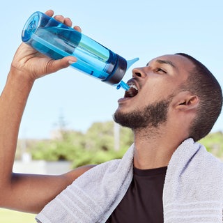 Ein Mann trinkt beim Training aus einer Wasserflasche: Ohne nachzudenken, schlucken wir etwa 2.000 Mal pro Tag: wenn wir essen und trinken oder den Speichel, der Mund und Zähne befeuchtet, in die Speiseröhre befördern und nicht in die Luftröhre. 