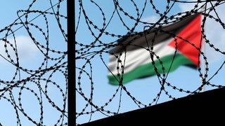 Flagge Palästinas an einem Grenzübergang hinter Stracheldraht: Seit über 100 Jahren kämpfen die Palästinenser um einen eigenen Staat. Doch die Probleme sind vielfältig.
