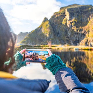 Handyaufnahme einer Bergkulisse auf den Lofoten: Reiseinfluencer berichten auf Instagram, TikTok und YouTube über ihre Trips. Sie zeigen paradiesische Strände, luxuriöse Hotels oder abgelegene Naturorte. Millionen Menschen lassen sich davon inspirieren.