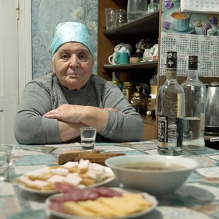 Ältere Frau sitzt an einem Esstisch: Was sind die Folgen der größten nuklearen Katastrophe unserer Zeit für Menschen und Tiere? Das erforschen Wissenschaftler, nachdem am 26. April 1986 in Tschernobyl Reaktor 4 explodiert war. 