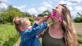 Kleines Mädchen kitzelt lachende Mutter mit Blumen: Warum sind wir kitzlig?