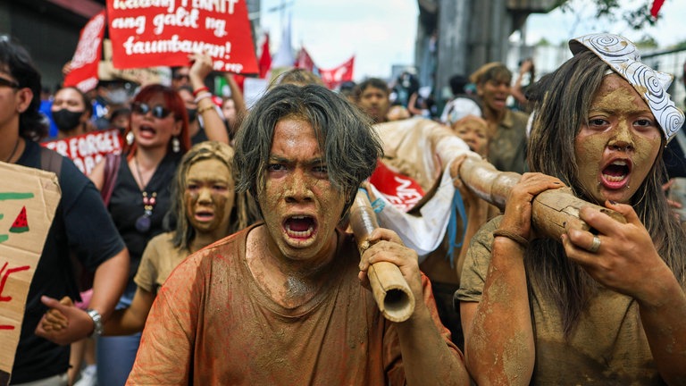 Junge Leute protestieren, mit Schlamm beschmutzt, in Manila gegen Korruption im Klimaschutz: Auf den Philippinen, wo Taifune immer mehr Lebensraum armer Menschen überfluten, flossen bereits Milliarden Euro in die Taschen von Politikern und Bauunternehmen.