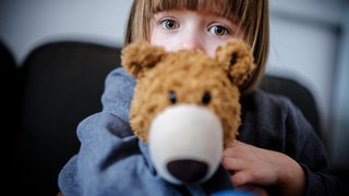 Verängstigtes Kind klammert sich an Teddybär: Viele Kinder entwickeln Ängste: vor Hunden, der Dunkelheit, der Schule oder der Trennung von den Eltern. Oft verschwinden die Ängste von selbst, doch manchmal bleiben sie und schränken das Leben ein. 