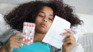 Kranke junge Frau lies Packungsbeilage ihres Medikaments: Antibiotika werden normalerweise mit Wasser eingenommen. Was passiert aber, wenn sie mit Milch eingenommen werden? Im Zweifel: Immer den Beipackzettel lesen!