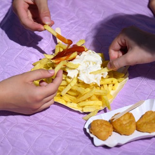 Symbolbild: Drei Mädchen teilen sich im Sommerbad Pommes Frites mit Ketchup und Mayonaise und Nuggets.