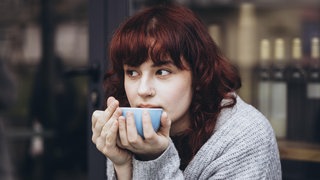 Junge Frau trinkt aus einer Tasse: Sind Tee und Kaffee Kalziumräuber und schlecht für die Knochen?