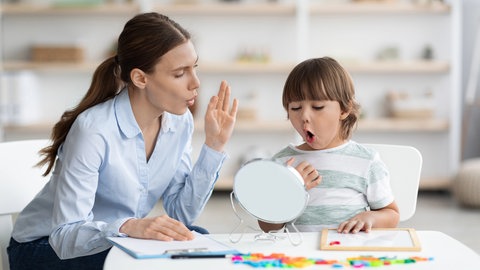 Kleiner Junge macht unter Anleitung einer Logopädin eine Sprechübung: Die Zahl der Kinder mit Sprachentwicklungsstörung steigt. Von Logopädie können aber auch Schlaganfall-Betroffene, Demenz-Erkrankte und sogar Säuglinge mit Fütterstörung profitieren.