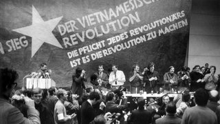 17.2.1968, Berlin: Etwa 3.000 Personen, meist Studenten, nehmen an der vom Sozialistischen Deutschen Studentenbund (SDS) durchgeführten "Internationalen Vietnam-Konferenz" in der TU teil. Auf dem Bild vor einer übergroßen Vietkong-Fahne am Tisch stehend sind zu sehen: (v.l.n.r.) K.D. Wolff (am Rednerpult), Dr. Klaus Meschkat, Dr. Johannes Agnoli, Christian Semmler, Gaston Salvatore, Rudi Dutschke, Günther Ament, Kurt Steinhaus und Tariq Ali
