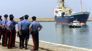 Italienische Polizisten schauen am 12. Juli 2004 auf das deutsche Rettungsschiff "Cap Anamur" beim Anlegen im sizilianischen Hafen Porto Empedocle