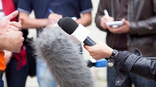 Journalisten umringen eine Person, viele schrieben, eine Person hält ein Mikrofon: Das SWR2 Archivradio sucht Audiobeiträge (Radio oder Podcast) aus dem Jahr 2021, die Radiogeschichte schreiben werden.