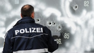 Einschusslöcher einer großkalibrigen Waffe markiert ein Polizist am 12.3.2009 in der Scheibe eines Autohauses in Wendlingen mit weißer Farbe. Auf dem Hof des Autohauses endete der Amoklauf eines 17-Jährigen, der zuvor 15 Menschen erschossen hatte, bevor er seinem Leben selbst ein Ende setzte. 